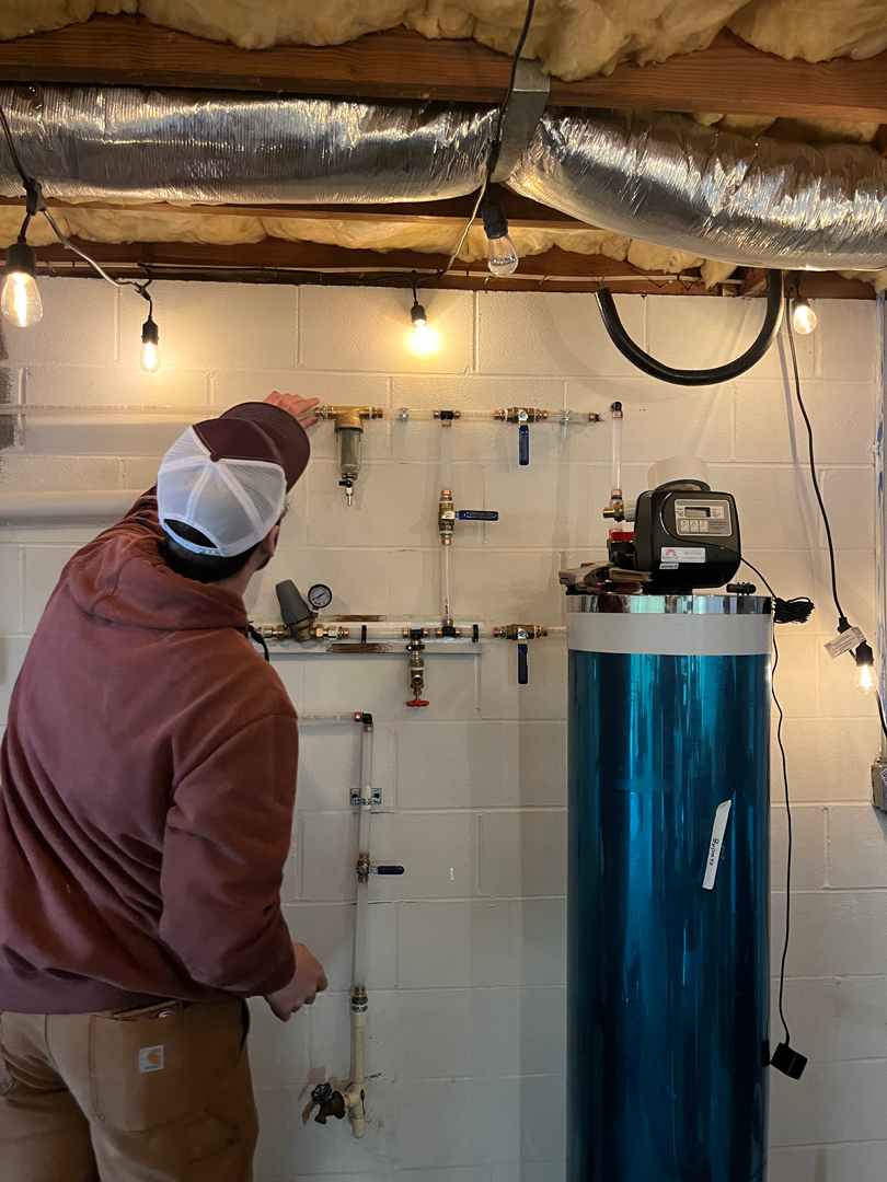 whole-home-water-filtration-system-installation-forest-city-nc Ohmstead Plumbing technician installing a whole-home water filtration and treatment system in a Forest City North Carolina basement to help protect against hard water, sediment, and well water issues common across Rutherford County homes.